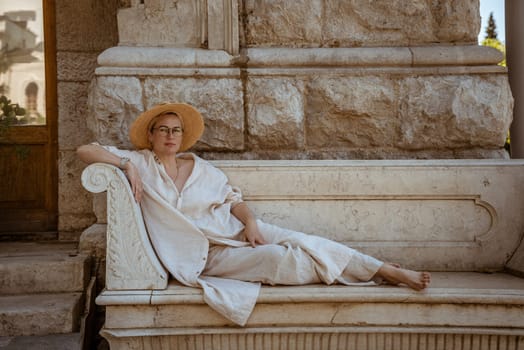 a beautiful mature woman sits on a stone bench in a hat and rests.