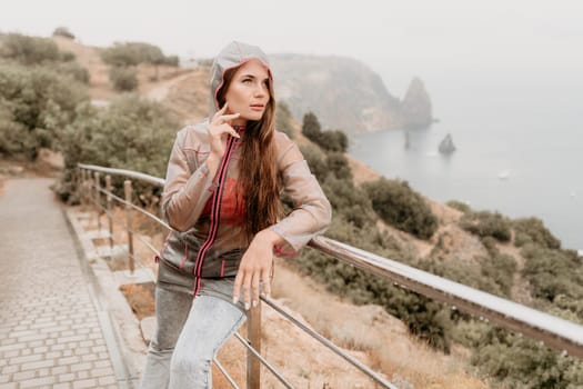 Woman rain park. Happy woman portrait wearing a raincoat with transparent umbrella outdoors on rainy day in park near sea. Girl on the nature on rainy overcast day