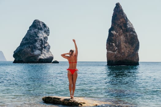 Woman travel sea. Young Happy woman in a long red dress posing on a beach near the sea on background of volcanic rocks, like in Iceland, sharing travel adventure journey