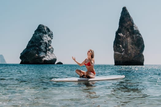 Close up shot of beautiful young caucasian woman with black hair and freckles looking at camera and smiling. Cute woman portrait in a pink bikini posing on a volcanic rock high above the sea