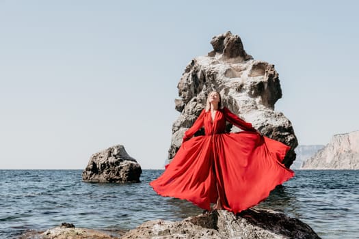 Woman travel sea. Young Happy woman in a long red dress posing on a beach near the sea on background of volcanic rocks, like in Iceland, sharing travel adventure journey