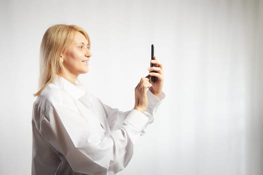 Portrait of a smiling casual woman holding smartphone over white background. The girl is chatting and taking selfies. Business lady with cell phone. Copy space