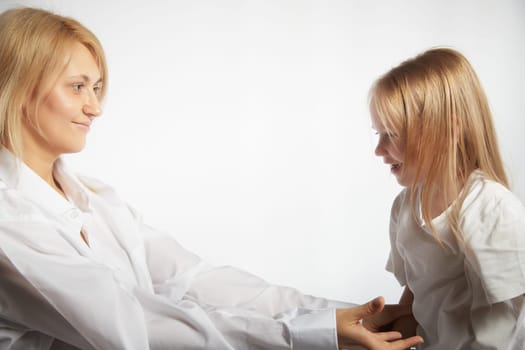 Portrait of blonde mother and daughter who having communicate and play on a white background. Mom and little girl models pose in the studio. The concept of love, friendship, caring in the family