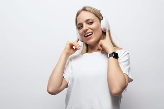 a girl in a white t-shirt listens to music in wireless headphones on a white background with empty space.