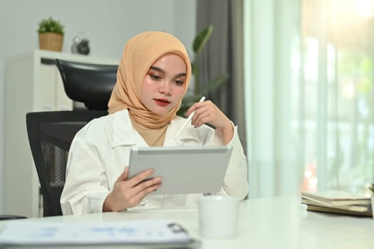 Attractive muslim woman entrepreneur making business plan while working on digital tablet at home office.