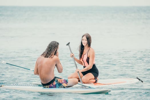 Sea woman and man on sup. Silhouette of happy young woman and man, surfing on SUP board, confident paddling through water surface. Idyllic sunset. Active lifestyle at sea or river