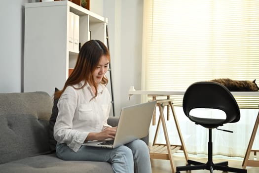 Young asian woman reading news online, checking social media on laptop at home. People, technology and lifestyle concept.