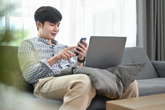 Smiling millennial man reading news online, checking social media on smart phone. People, technology and lifestyle concept.