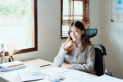 Portrait of a woman business owner showing a happy smiling face as he has successfully invested her business using computers and financial budget documents at work.