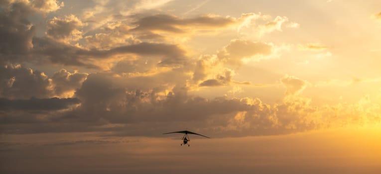 Propeller plane flies in the sunset sky. Banner, A small private hang-glider in a cloudy sky