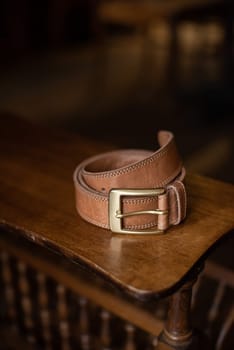 Brown leather belt with golden buckle on a wooden surface.