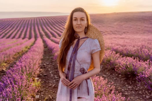 Woman lavender field sunset. Romantic woman walks through the lavender fields. illuminated by sunset sunlight. She is wearing a pink dress with a hat