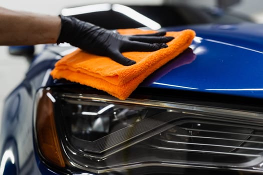 Hand car drying with microfiber in detailing auto service. Cleaner worker dry body car after washing automobile