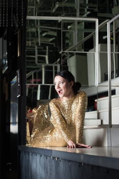 Beauty woman in sexy gold dress posing on bar table