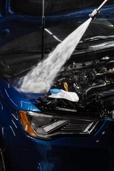 Detailing cleaning motor from dust and dirt. Pouring water on car engine. Washing car engine with spray, brush and detergent in detailing auto service