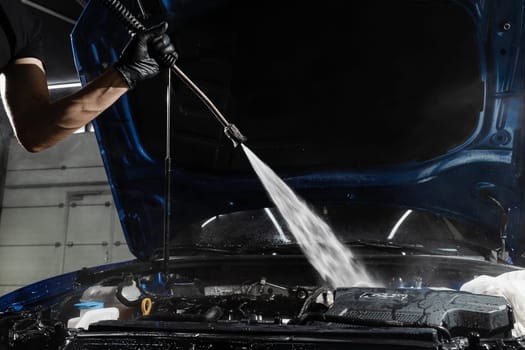 Washing car engine with with water in detailing auto service. Detailing cleaning motor from dust and dirt. Pouring water on car engine