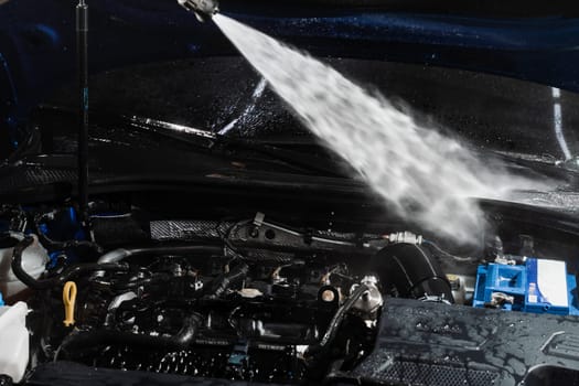 Washing car engine with with water in detailing auto service. Detailing cleaning motor from dust and dirt. Pouring water on car engine