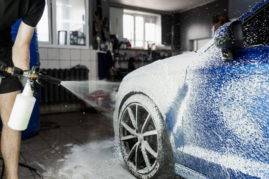 Second phase of detailing washing in car service. Car washer does full body car wash. Process of spraying foam on the car body in the garage