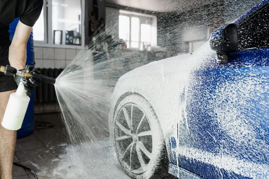 Second phase of detailing washing in car service. Car washer does full body car wash. Process of spraying foam on the car body in the garage