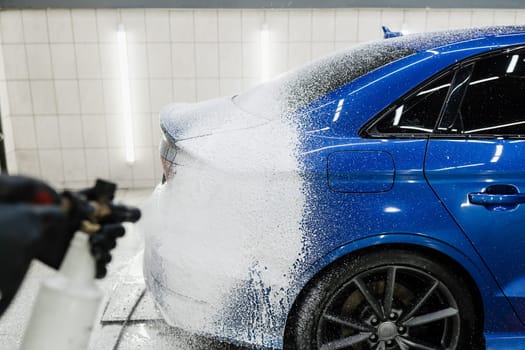 Second phase of detailing washing in car service. Car washer does full body car wash. Process of spraying foam on the car body in the garage