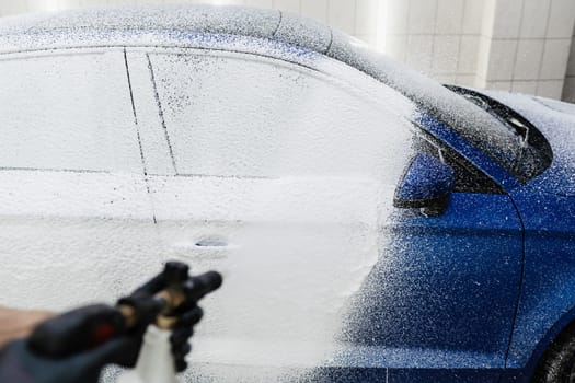 Car washer does full body car wash. Process of spraying foam on the car body in the garage. Second phase of detailing washing in car service