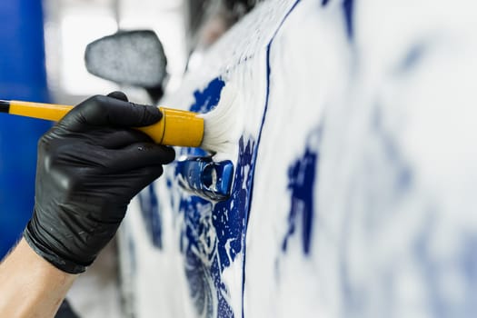 Hand brush washing of car body with foam in car detailing service. Car wash worker washes a car body