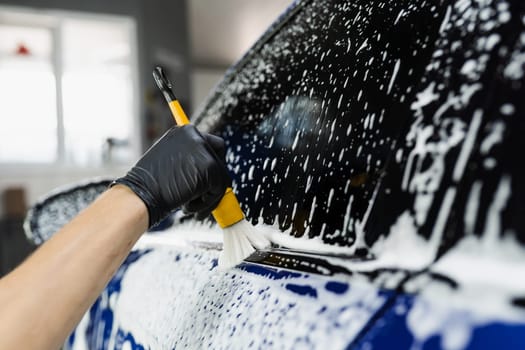 Hand brush washing of car body with foam in car detailing service. Car wash worker washes a car body