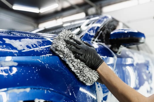 Hand washing with microfiber glove with foam car body in garage. Car washer doing manual foam washing in auto detailing service