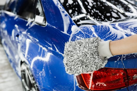 Hand washing with microfiber glove with foam car body in garage. Car washer doing manual foam washing in auto detailing service