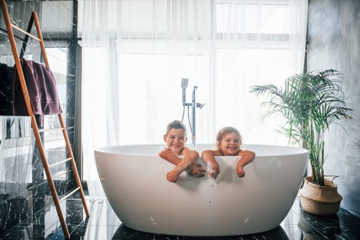 Two kids having fun and washing themselves in the bath at home. Posing for a camera.