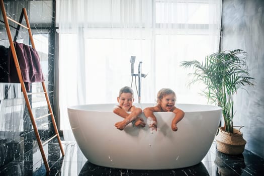 Two kids having fun and washing themselves in the bath at home. Posing for a camera.