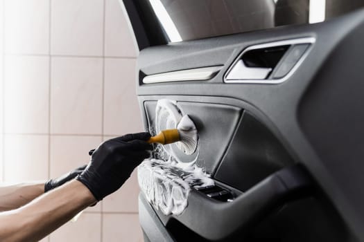 Process of foam and detergent cleaning with brush inside handle of car door. Car detailing service. Worker in cleaning service washing leather interior of clients auto