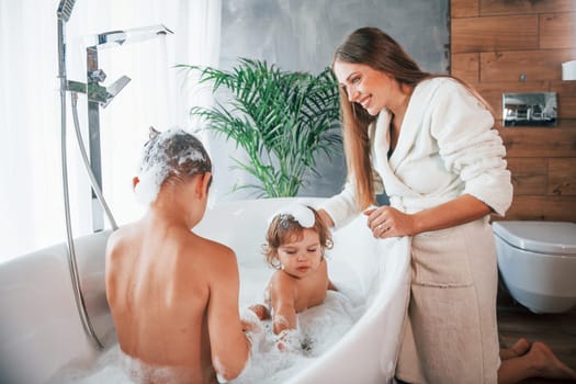 Having fun. Young mother helps her son and daughter. Two kids washing in the bath.