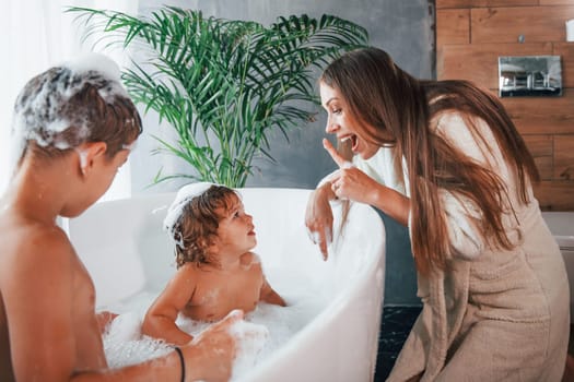 Having fun. Young mother helps her son and daughter. Two kids washing in the bath.