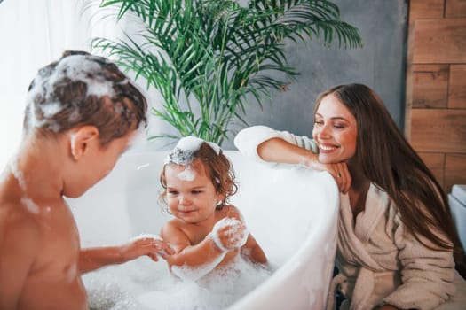 Having fun. Young mother helps her son and daughter. Two kids washing in the bath.