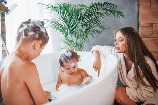Having fun. Young mother helps her son and daughter. Two kids washing in the bath.