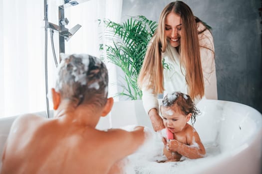 Having fun. Young mother helps her son and daughter. Two kids washing in the bath.