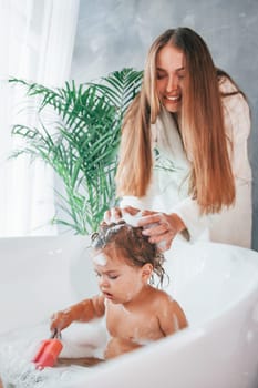 Young mother helps her daughter to wash in the bath.