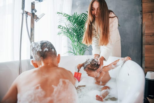 Having fun. Young mother helps her son and daughter. Two kids washing in the bath.