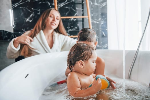 Having fun. Young mother helps her son and daughter. Two kids washing in the bath.