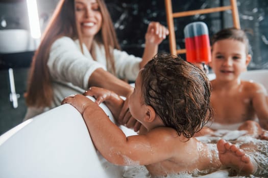 Young mother helps her son and daughter. Two kids washing in the bath.