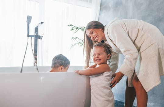 After washing. Young mother helps her son and daughter.