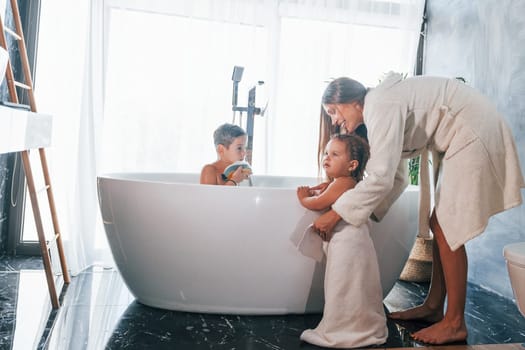 After washing. Young mother helps her son and daughter.