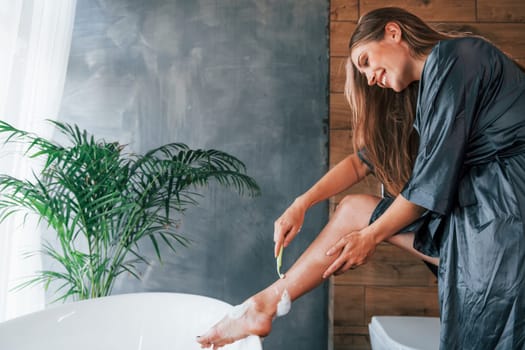 Beautiful young woman have free time at home in the bath. Shaves legs.