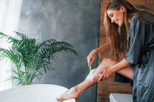 Beautiful young woman have free time at home in the bath. Shaves legs.