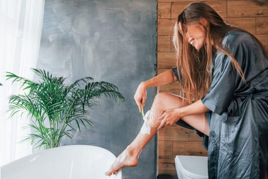 Beautiful young woman have free time at home in the bath. Shaves legs.