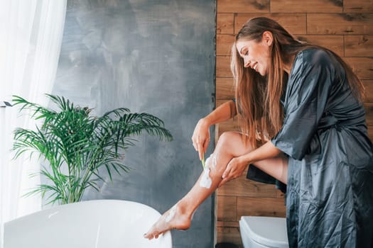 Beautiful young woman have free time at home in the bath. Shaves legs.
