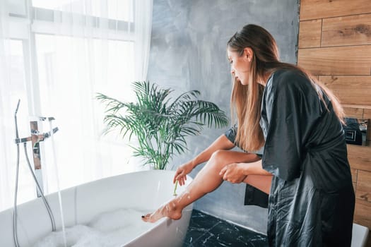 Beautiful young woman have free time at home in the bath. Shaves legs.