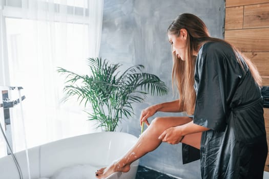 Beautiful young woman have free time at home in the bath. Shaves legs.