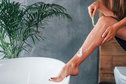 Beautiful young woman have free time at home in the bath. Shaves legs.
